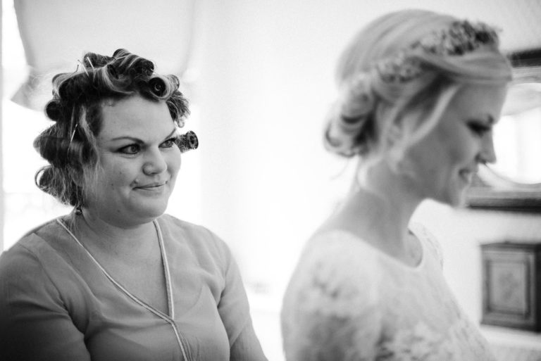 Brautschwester noch mit Haarwicklern im Haar, hilft der Braut beim anziehen des Kleides.