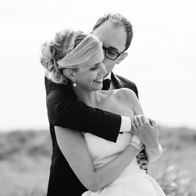 Hochzeitsfotografie Sankt-Peter Ording- Hochzeitsbilder am Strand- Bräutigam umarmt Braut von hinten und küsst sie auf die Wange.