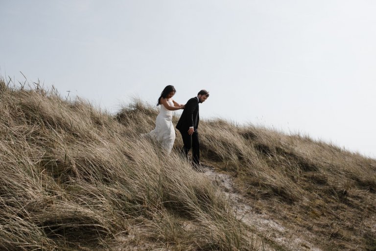 Sankt-Peter-Ording- Hochzeitsbilder- Mit Blick auf die Dünen. Brautpaar auf dem Weg zum Meer.