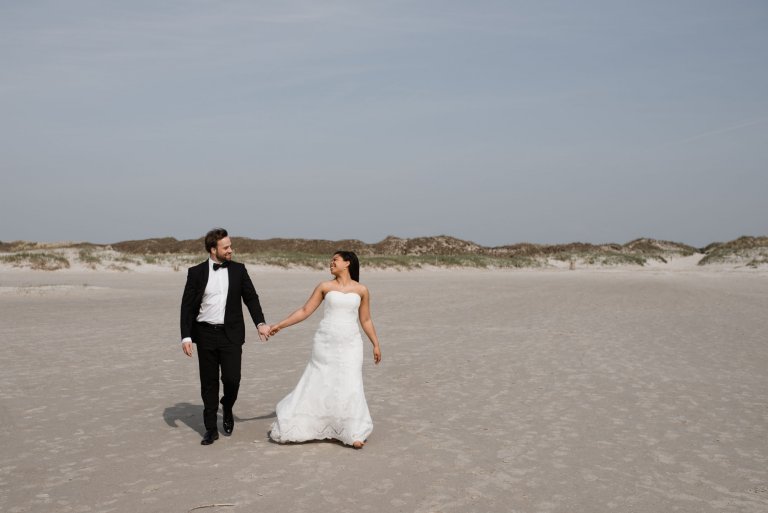 Sankt-Peter-Ording- Hochzeitsbilder- Hochzeitspaar geht Hand in Hand den Strand entlang.