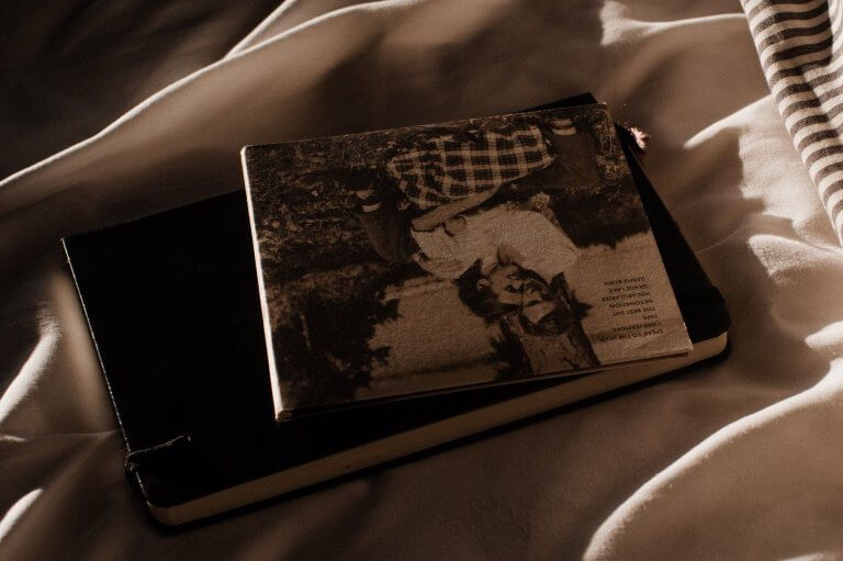 Eine CD und eine Tagebuch liegen übereinander auf einer Decke. Das komplette Bild ist in sehr warmen Tönen gehalten. Vermutlich wurde es an einem Abend aufgenommen. Auf der CD ist ein Paar zu sehen.