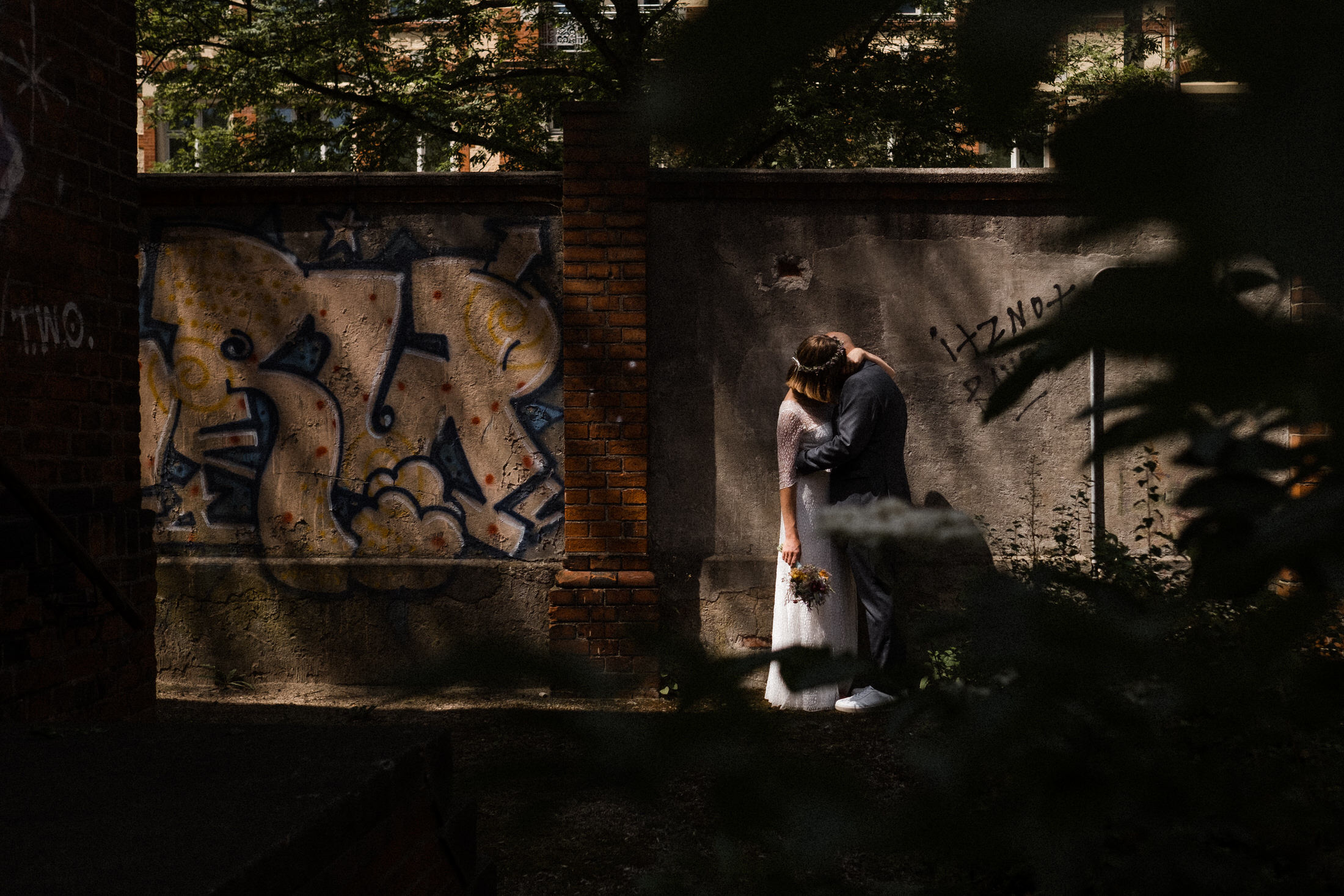 Brautpaar küsst sich vor einer Graffiti Wand.