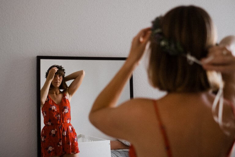 Braut setzt sich, vor dem Spiegel stehend, den Blumenkranz auf.