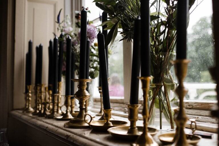 auf der Fensterbank in der Villa stehen goldene Kerzenhalter mit grünen Stabkerzen, dahinter stehen sind Blumenvasen