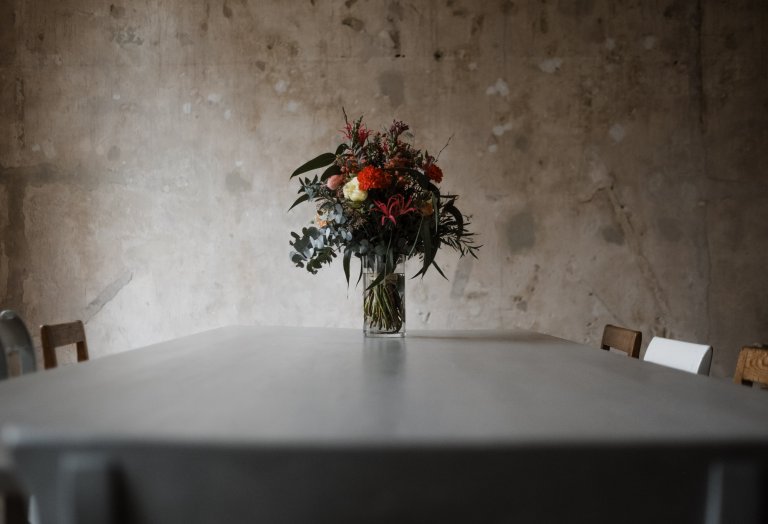 Brautmode Hamburg- AveevA- in dem Zimmer in Haller 6 steht ein Tisch, auf dem ein Blumenstrauß in einer Vase steht, die Wand dahinter hat eine naturbelassene Wandoberfläche