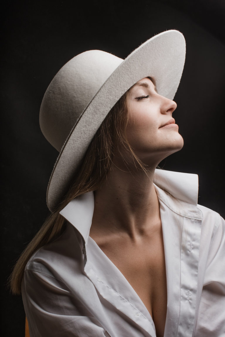 Editorial- Rotkäppchen Design- Portrait Hutmanufaktur- weißer Hut Model Das Gesicht in Richtung Licht gewendet.