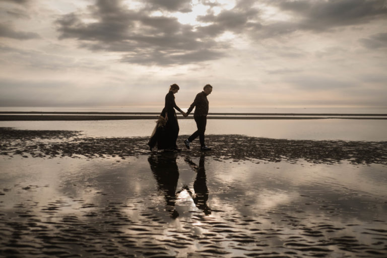 Hochzeitsfotografie-Sankt-Peter-Ording - Hochzeitspaar geht hintereinander den Strande entlang und spiegeln sich in einem Priel