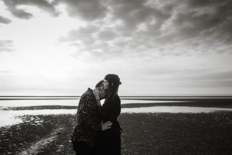 Hochzeitsfotografie-Sankt-Peter-Ording - schwarz/weiß Aufnahme des Hochzeitspaares im Hintergrund die Nordsee