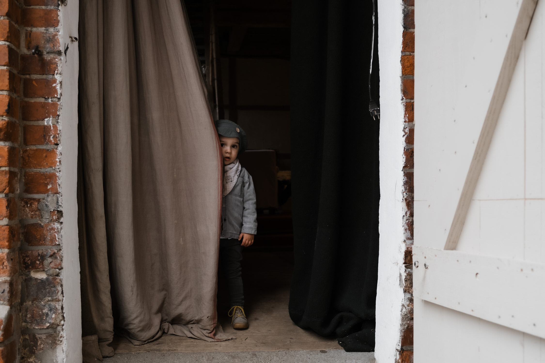 Hochzeitsfotografie Gut Mönkhof- Kind versteckt sich hinter einem Türvorhang